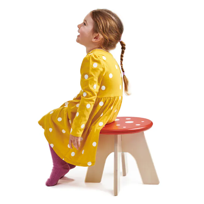 Tender Leaf Toadstool - 6 - Yellow polka dot dress, child sitting, red stool, wooden legs, purple socks, braided hair, white