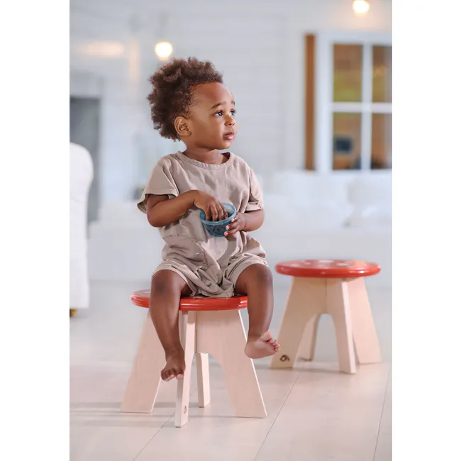 Tender Leaf Toadstool - 4 - Cute toddler sitting on red stool, holding blue bowl, curly hair, beige outfit, indoor setting