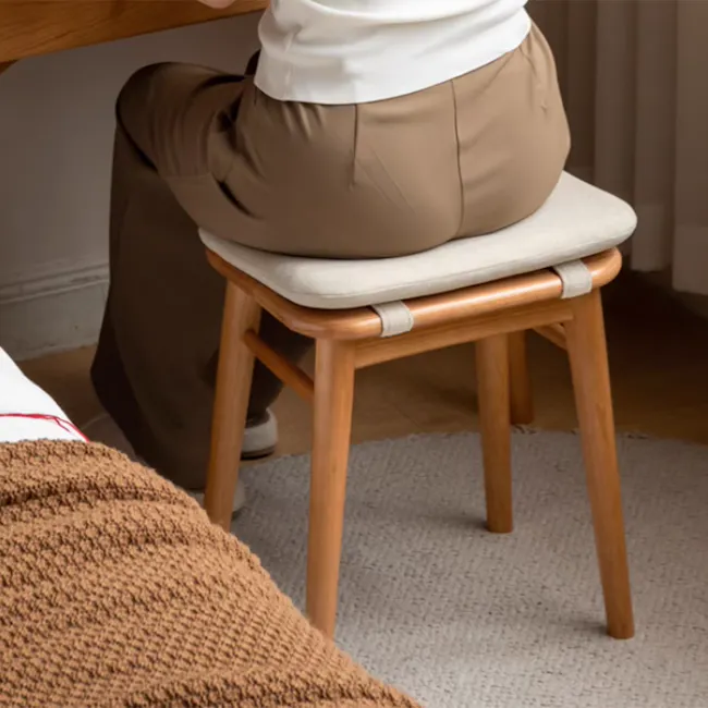 Haku Stool - 2 - wooden stool, beige cushion, person sitting, brown pants, white shirt, wooden frame, cozy room, soft