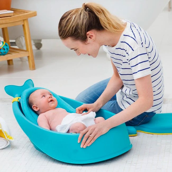 Skip Hop Moby Smart Sling 3 Stage Bath - Blue - 7 - Baby in blue carrier, woman holding baby, white towel on baby, striped