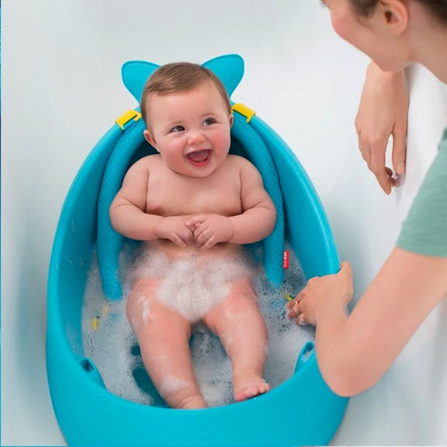 Skip Hop Moby Smart Sling 3 Stage Bath - Blue - 8 - Baby in blue bath seat, smiling, sitting in bubble-filled tub, wearing