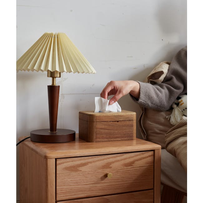 Kenji Tissue Box - 2 - Vintage lamp with beige shade, wooden nightstand, brown wooden drawer, person's hand holding tissue