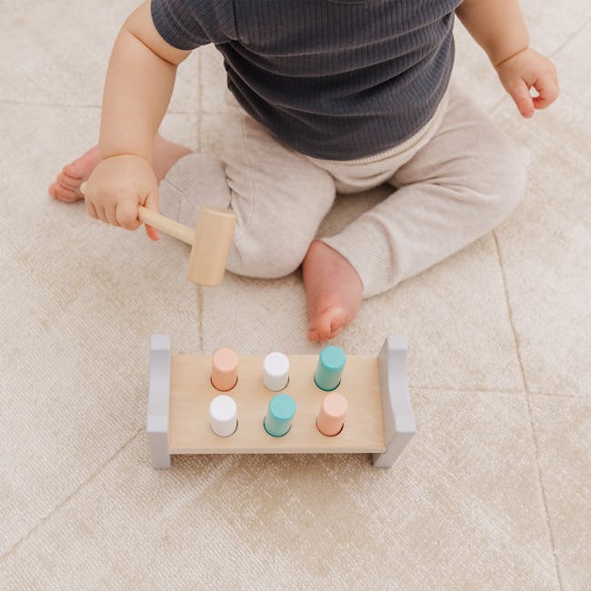 Bubble Wooden Hammer Bench - 4 - Baby playing with wooden toy, holding wooden mallet, colorful buttons on toy, beige carpet