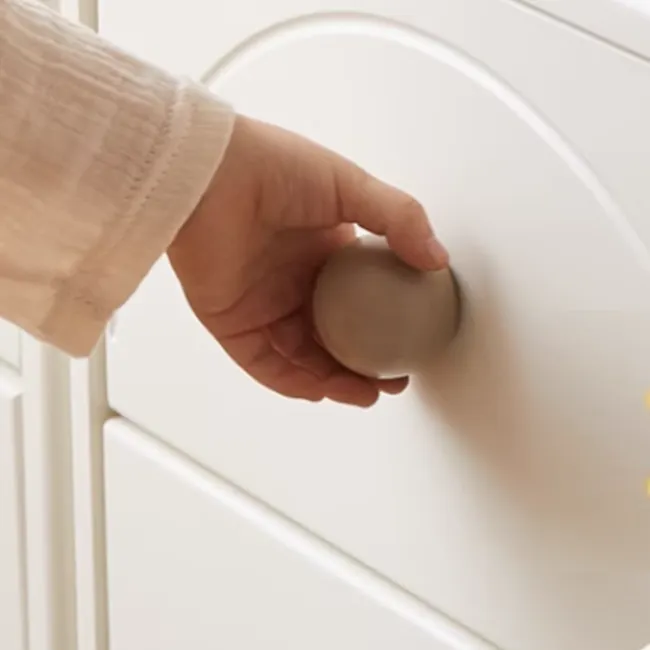 Mika Kids 2 Door Cabinet - 10 - Hand holding smooth, round, beige ball, white door with subtle curves, soft, natural
