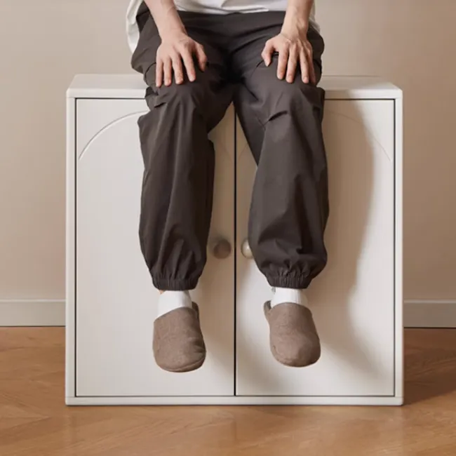 Mika Kids 2 Door Cabinet - 8 - White cabinet, person sitting, brown slippers, gray pants, white socks, wooden floor